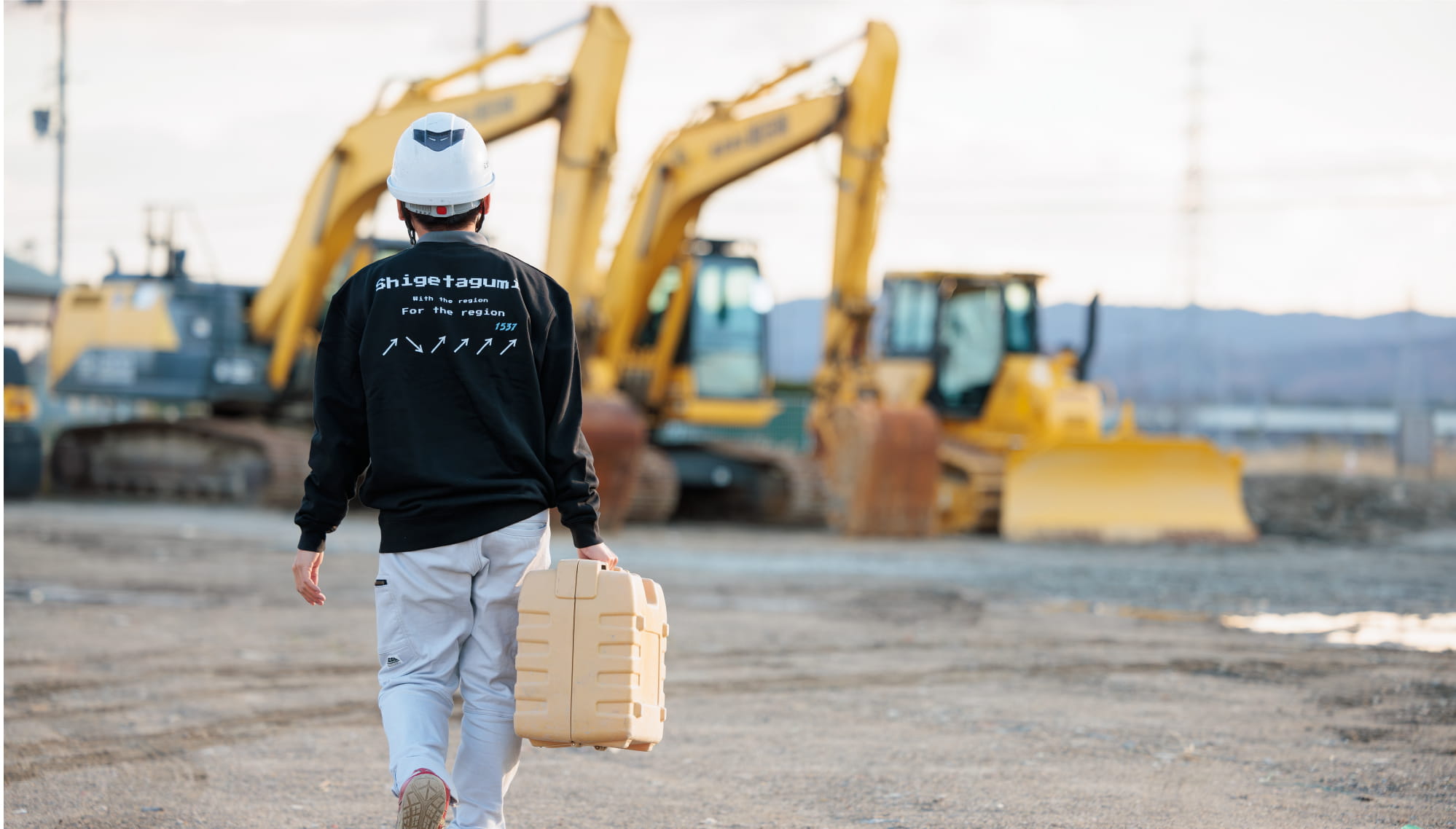 建設現場でヘルメットをかぶった作業員が機材を持って歩いている後ろ姿