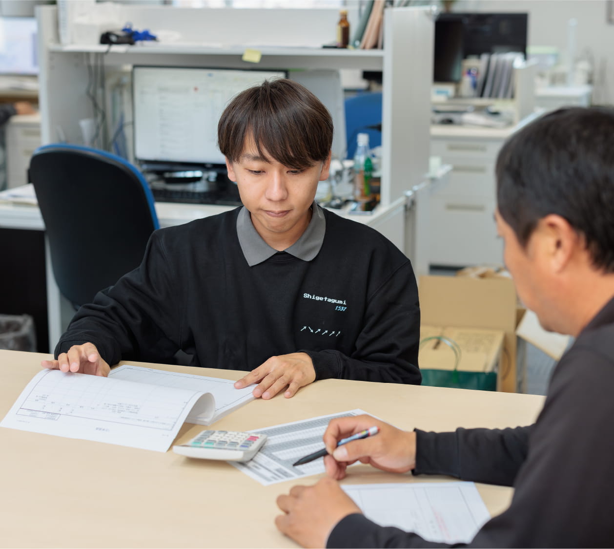 オフィス内で2人の男性が資料を見ながら打ち合わせをしている様子