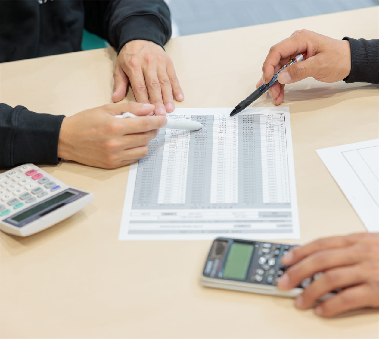 机の上で2人がペンを使いながら資料を指し示して議論している様子。