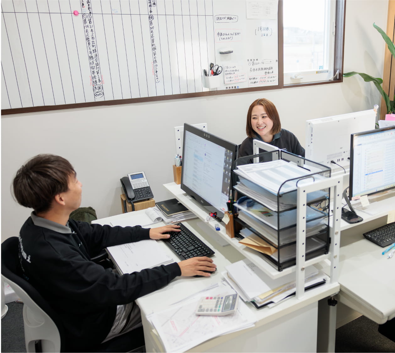 2人の社員がオフィスでパソコンを操作しながらコミュニケーションを取っている様子