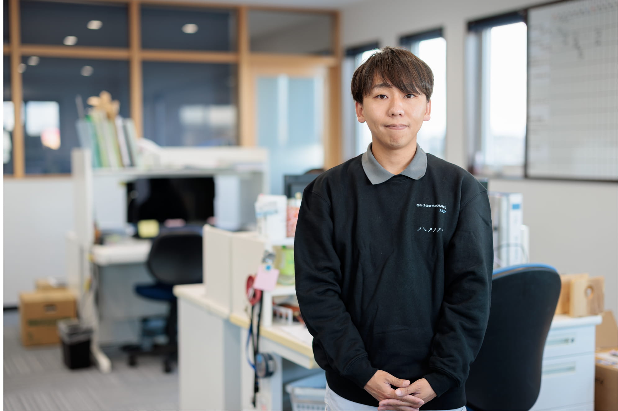 オフィスで黒い制服を着た男性が落ち着いた表情でこちらを見つめる様子