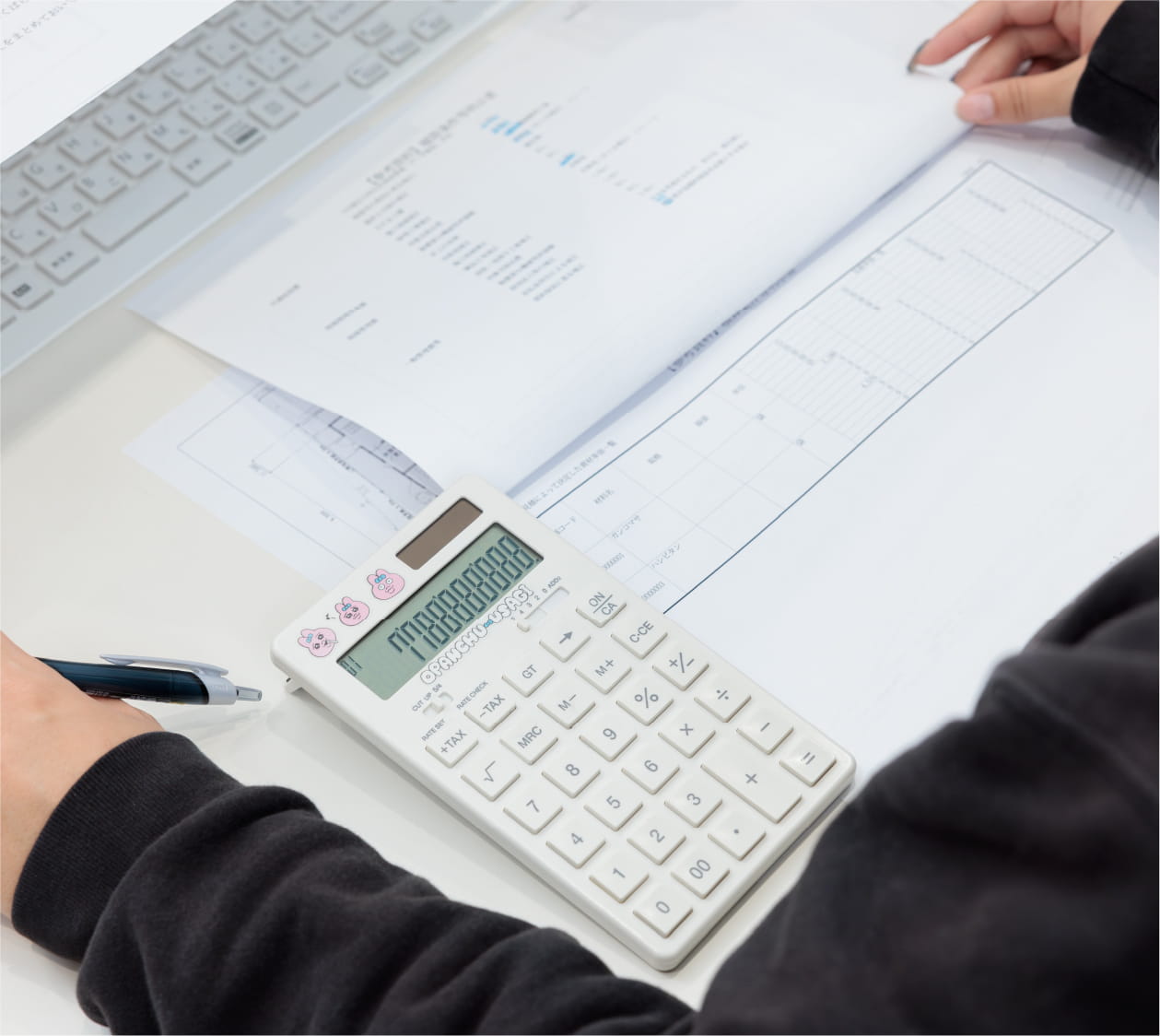 女性がオフィスで設計図を見ながら電卓を使い、計算や作業をしている様子