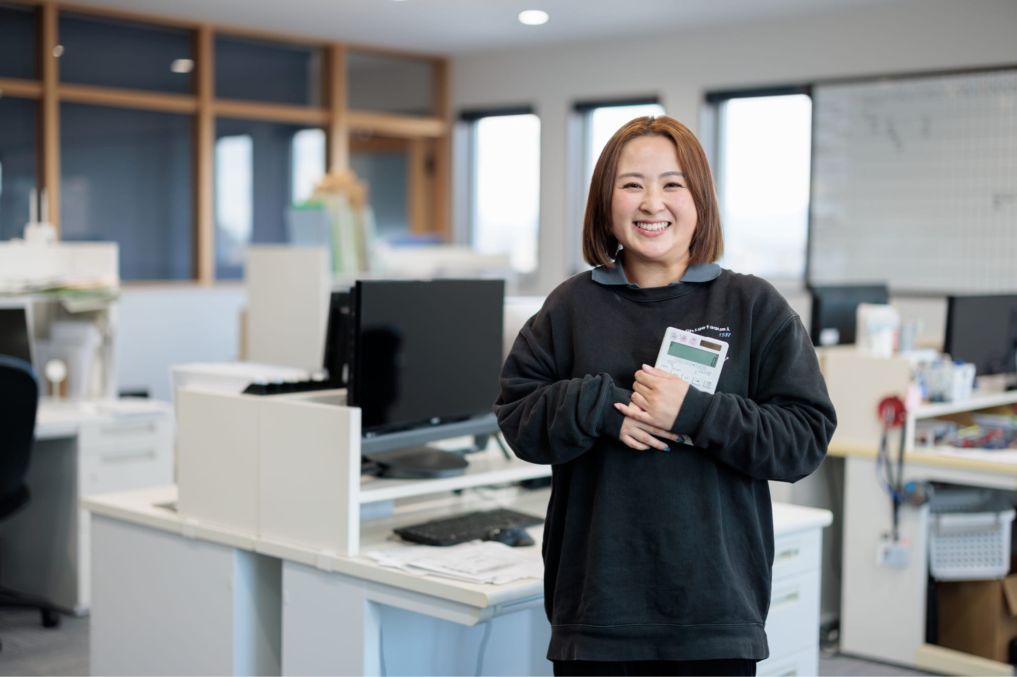 黒い制服を着た女性が笑顔で電卓を持ち、嬉しそうな表情をしている様子