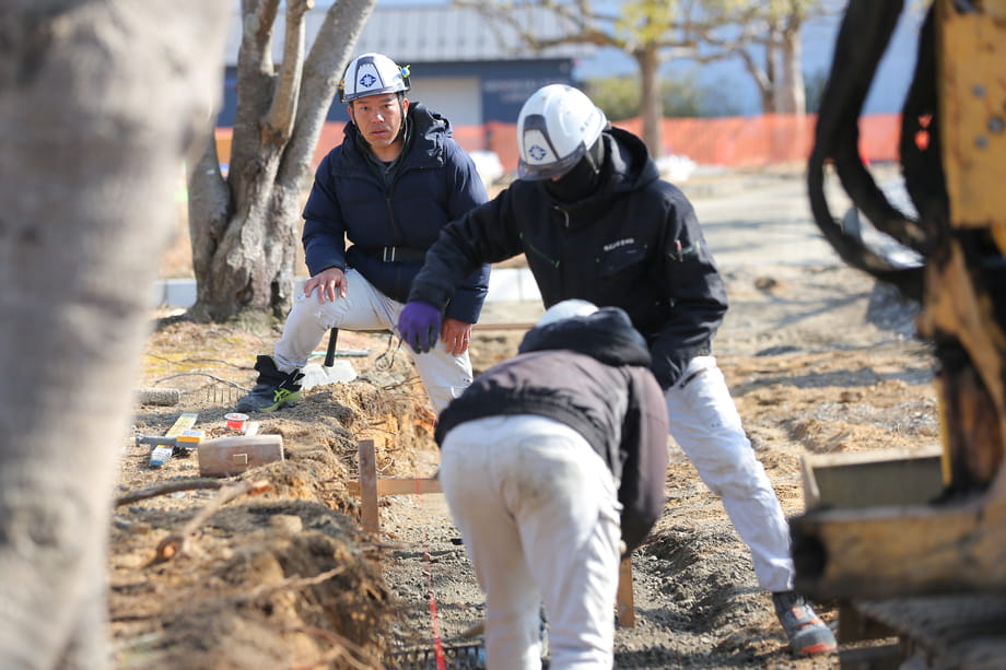 工事現場で3人の作業員が協力しながら作業を進めている様子
