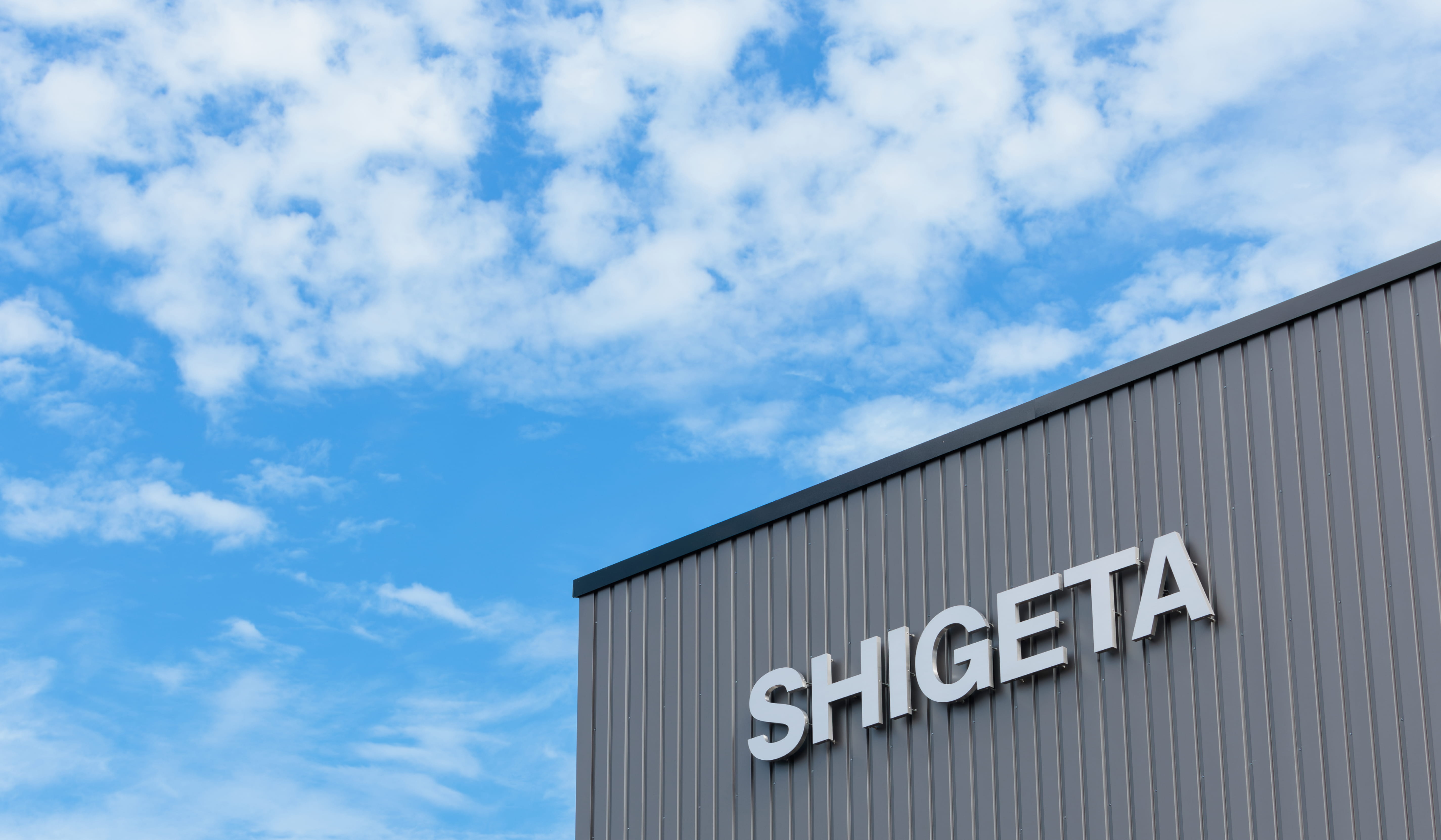 青空の下、建物の外壁に「SHIGETA」の文字が取り付けられている