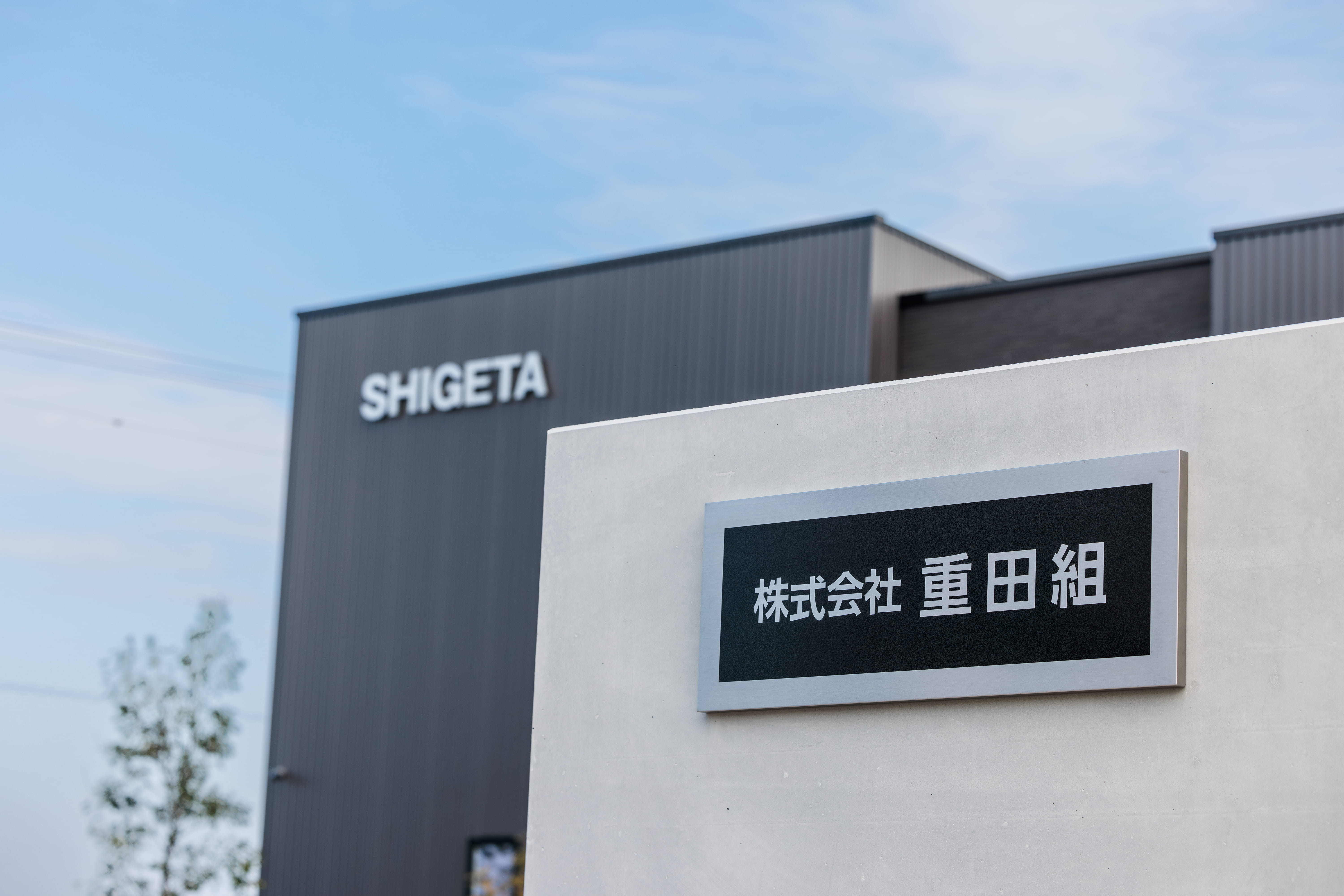 コンクリートの壁に「株式会社 重田組」の表札が取り付けられている