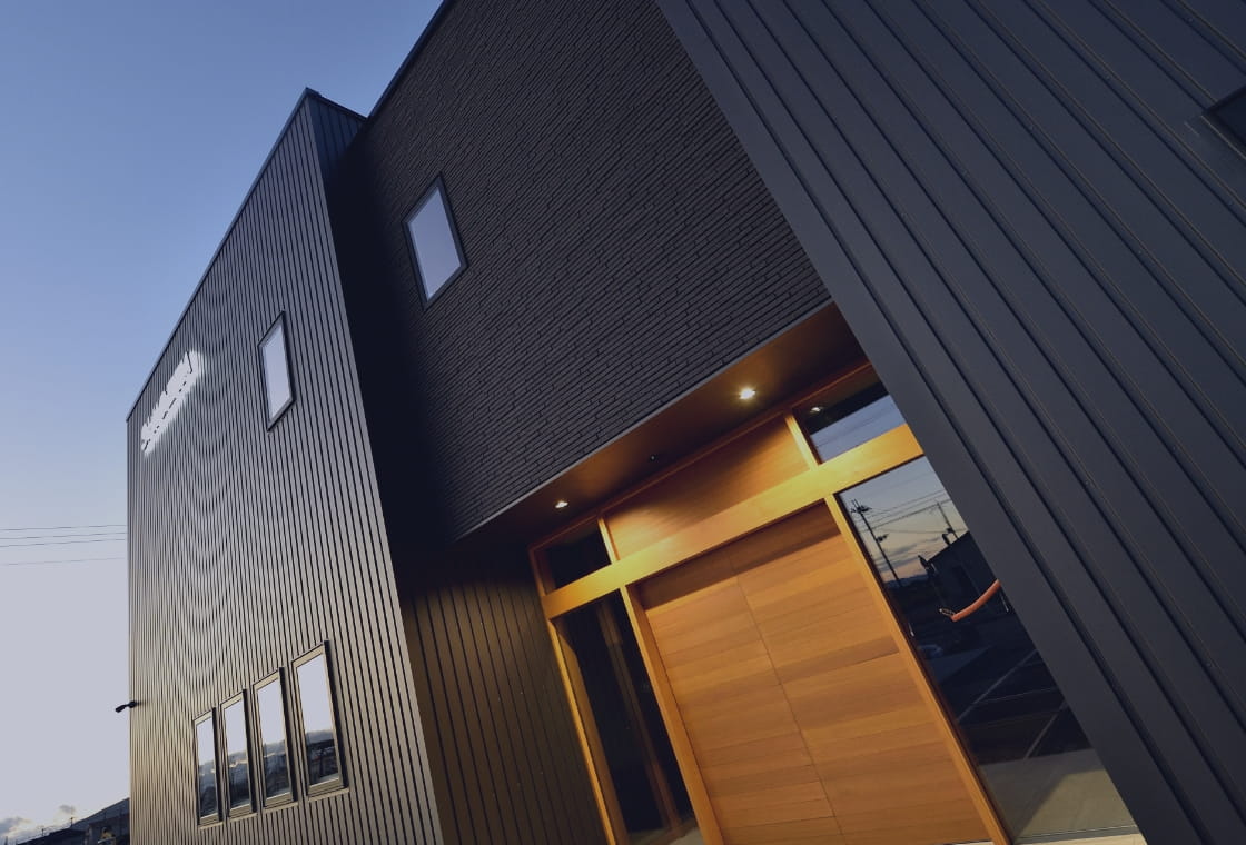 黒い外壁と木製の扉が特徴的な重田組のオフィスを斜めから撮影した写真