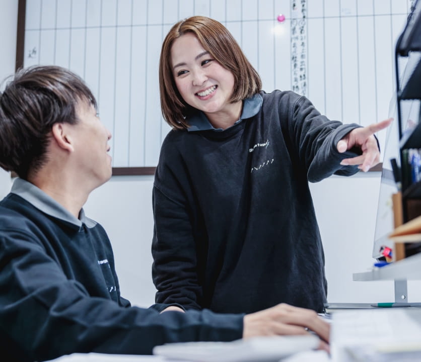 オフィスで女性が指をさしながら笑顔で男性と会話しているシーン