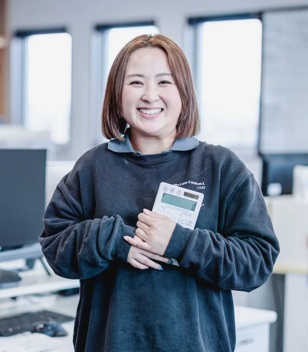 黒い制服を着た女性が笑顔で電卓を持ち、嬉しそうな表情をしている様子