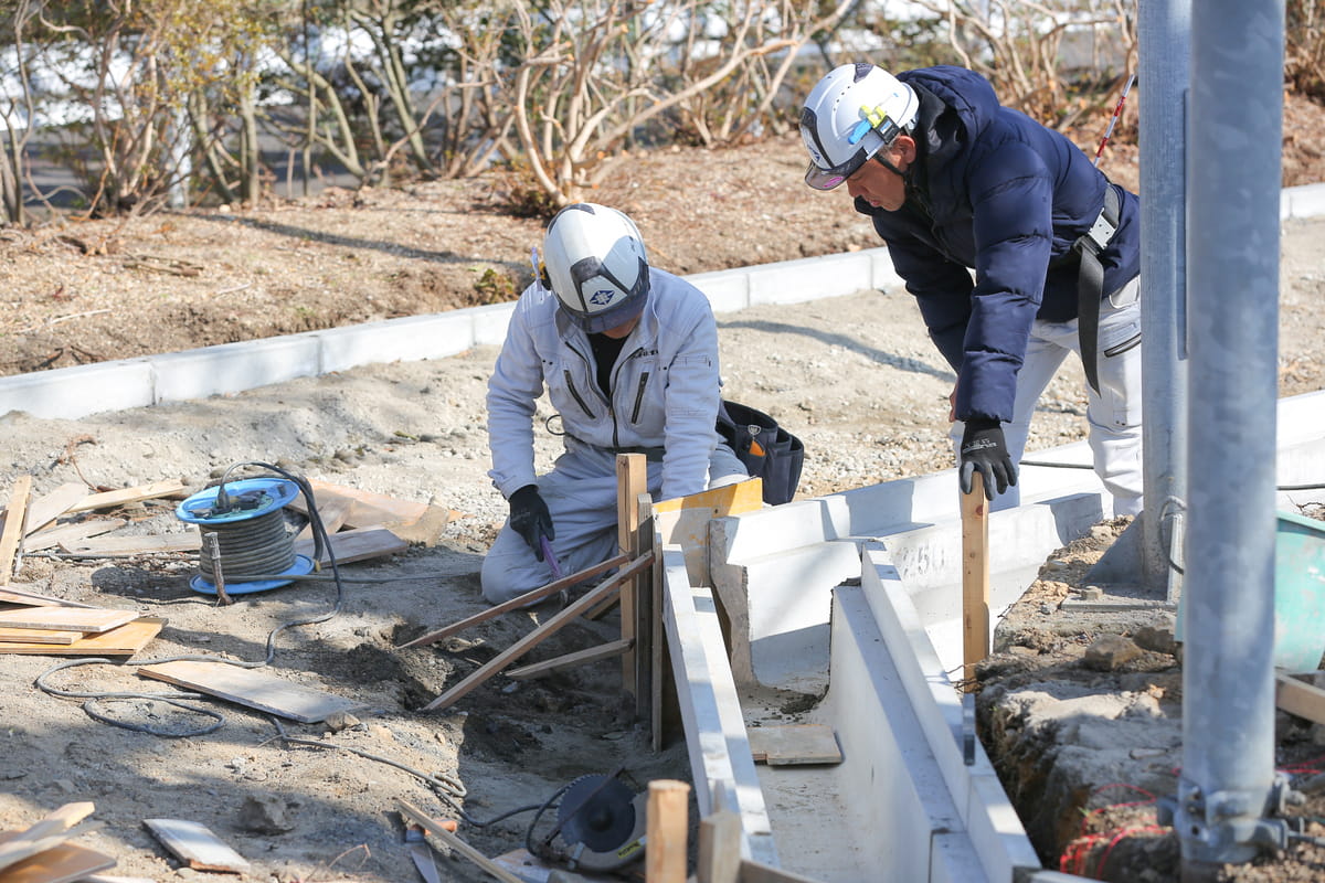 ヘルメットを着用した作業員がコンクリート舗装の仕上げと測定を行う場面