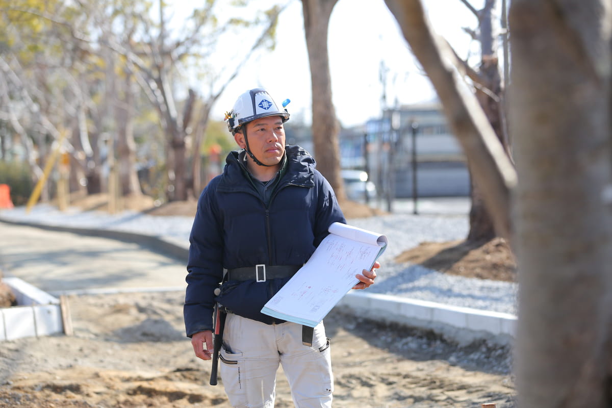 工事現場でヘルメットを着用し、設計図を持ちながら進捗を確認する作業員